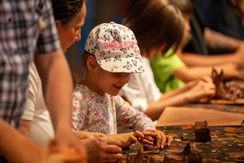 Uczestnicy podczas lepienia z gliny. Zbliżenie na dziewczynkę w czapce z daszkiem.