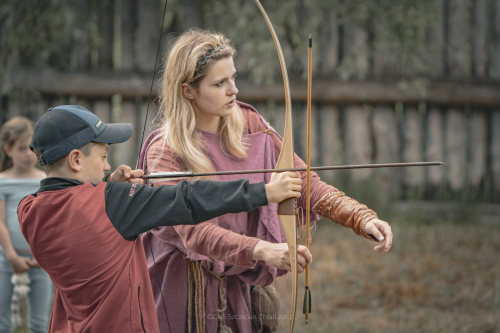 Chłopiec próbuje strzelać z łuku, obok pani instruktorka