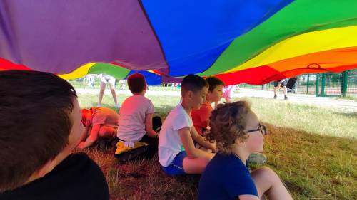 Dzieci siedzą na trawie, nad głowami mają rozwiniętą chustę animacyjną