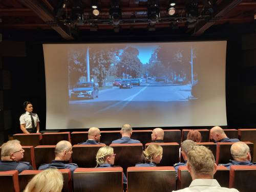 Widok na ekran zza pleców osób siedzących na sali kinowej.