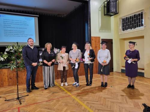 Na zdjęciu mężczyzna, koordynatorka UTW oraz słuchaczki w biretach na głowie i indeksami w dłoniach